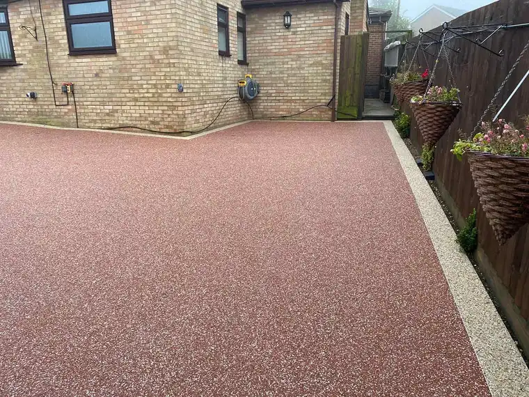 Red resin bound path with gravel border beside a stone house