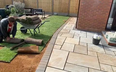 Laying fresh turf rolls beside a new patio