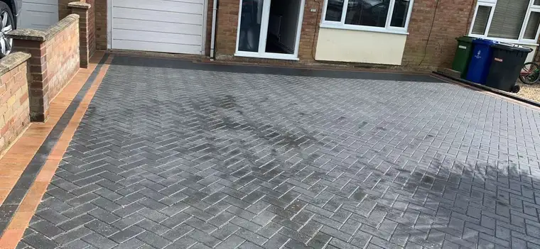Charcoal block paving with contrasting edging by a brick wall